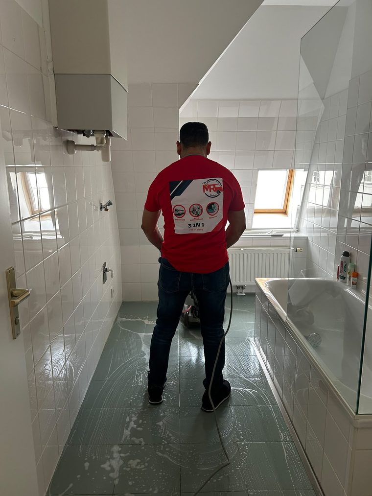 Reinigungskraft reinigt einen gefliesten Badezimmerboden mit einer Einscheibenmaschine