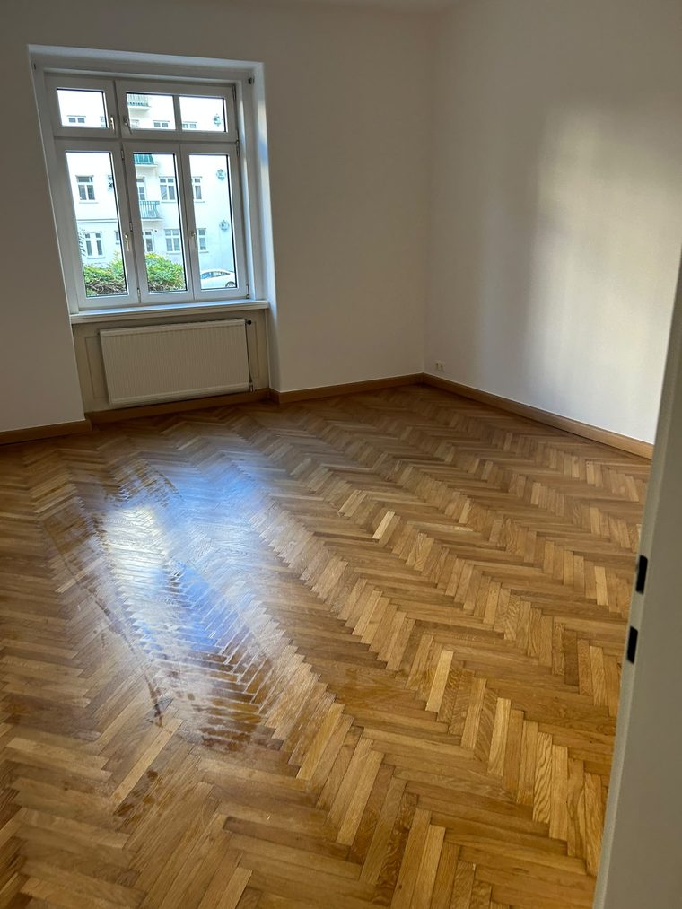 Leergeräumtes Zimmer mit Fischgrätparkett, Fenster und Heizkörper