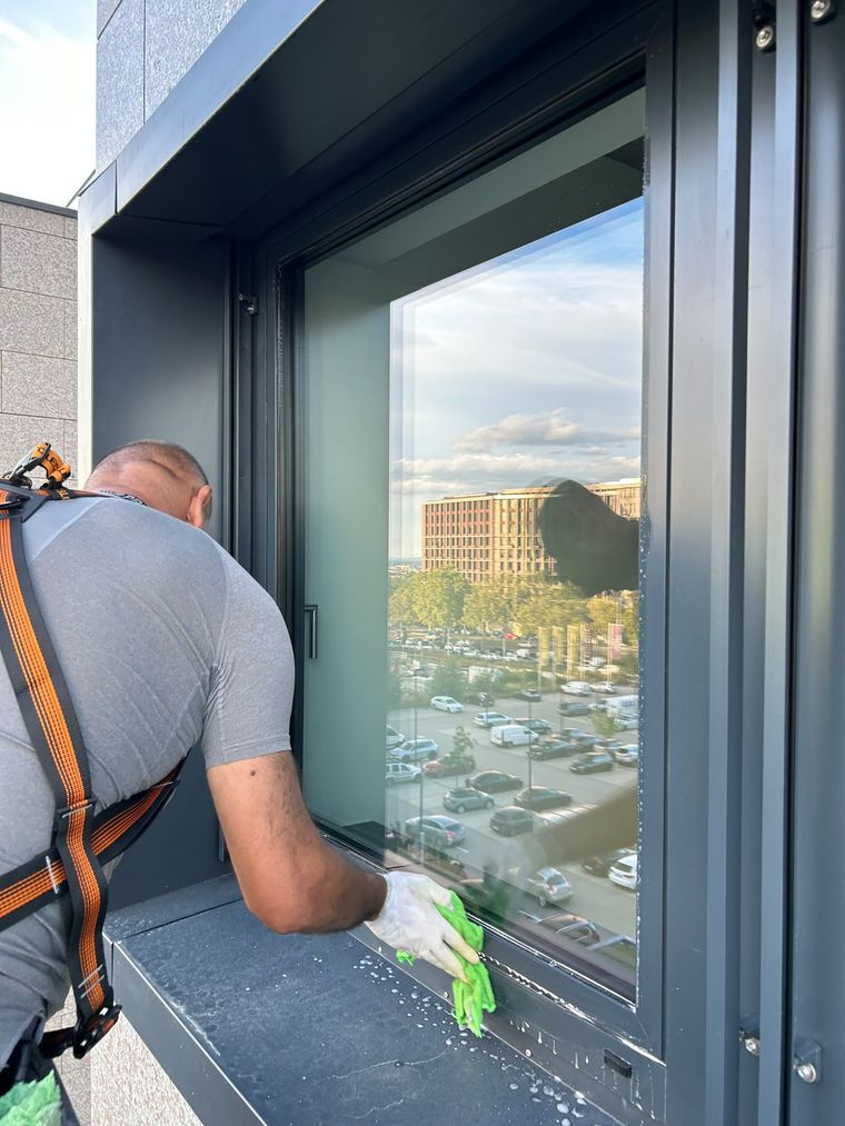 Reinigungskraft reinigt ein Fenster von außen und wischt Rahmen und Falz nach