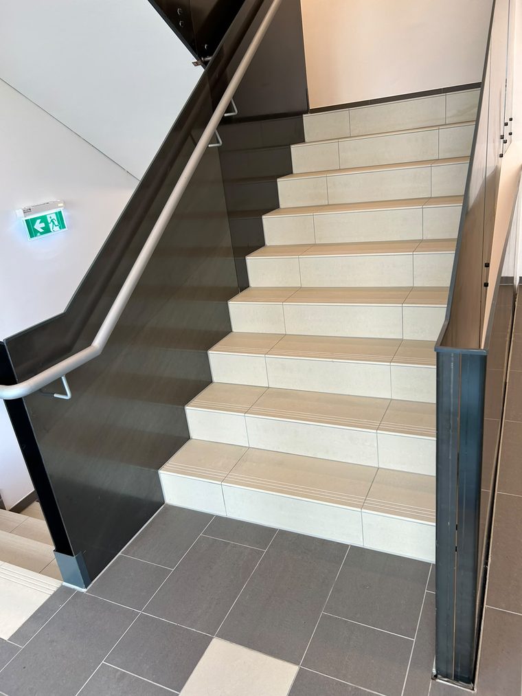 Gereinigtes Stiegenhaus mit hellen Fliesenstufen, Handlauf und Glasbrüstung