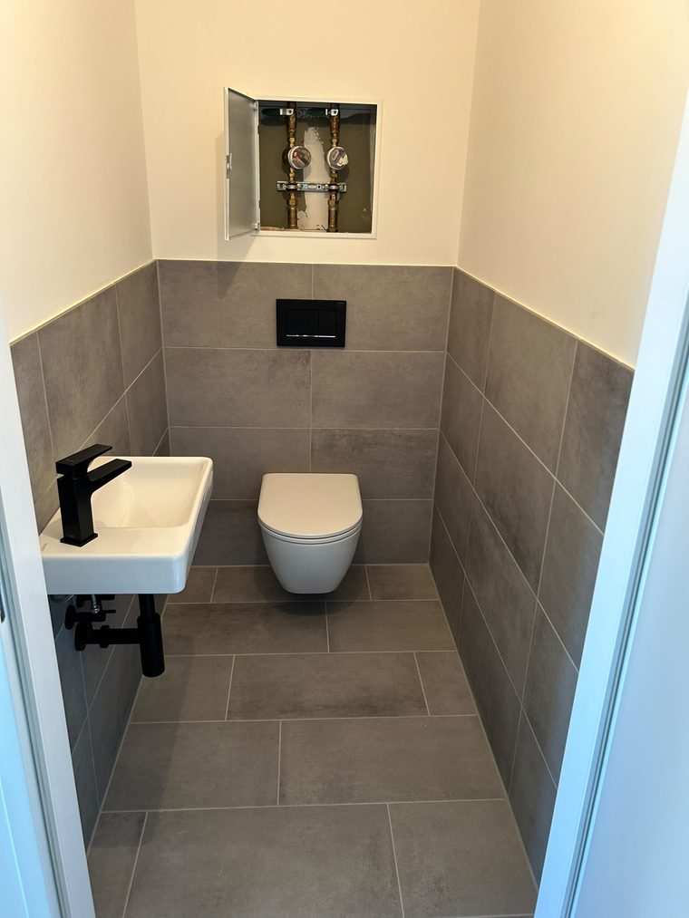 Kleiner Sanitärraum mit Waschbecken, Wand-WC und grauen Fliesen nach der Reinigung