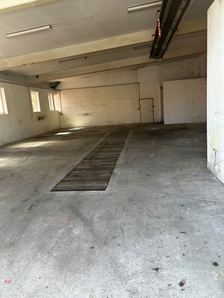 Leere Werkhalle mit Betonboden, abgedecktem Bodenkanal und Lichtbändern an der Decke