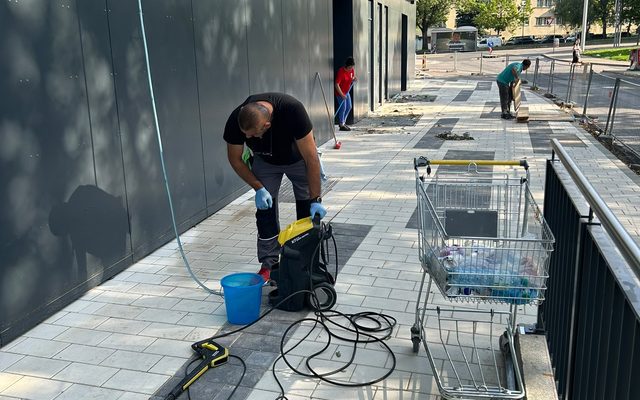 Reinigungskraft mit Hochdruckreiniger vor einer Metallfassade
