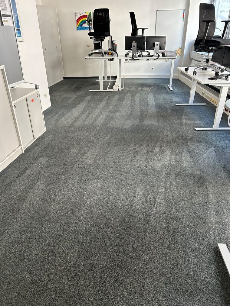 Büro mit grauem Teppichboden und Arbeitsplätzen während der Reinigung