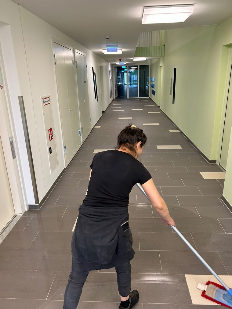 Reinigungskraft wischt den Gang einer Schule mit einem Flachmopp