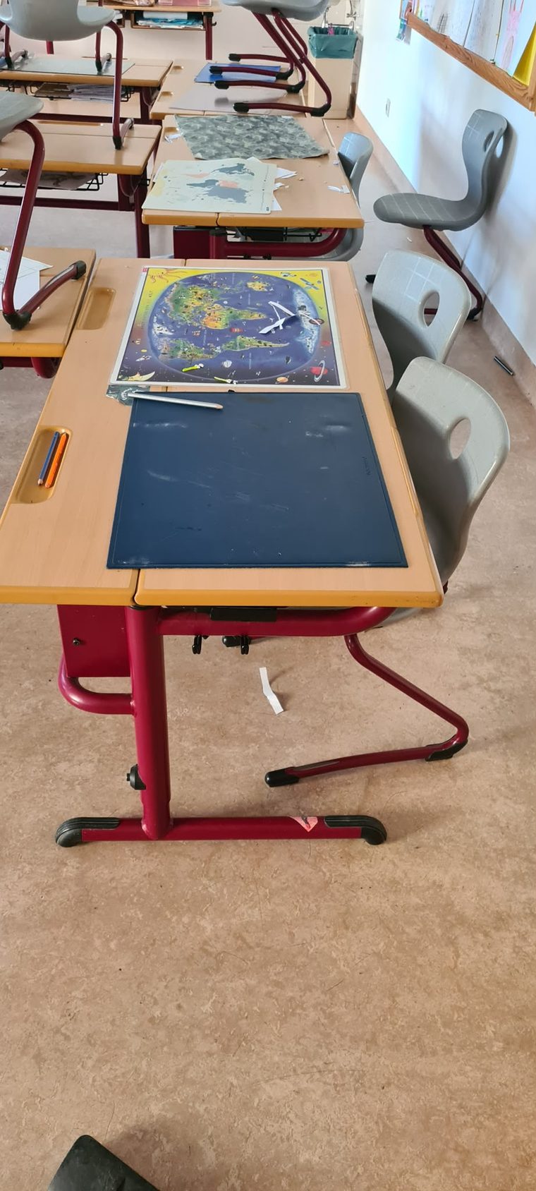 Schultisch mit Weltkarte und dunkler Schreibunterlage, daneben ein Sessel